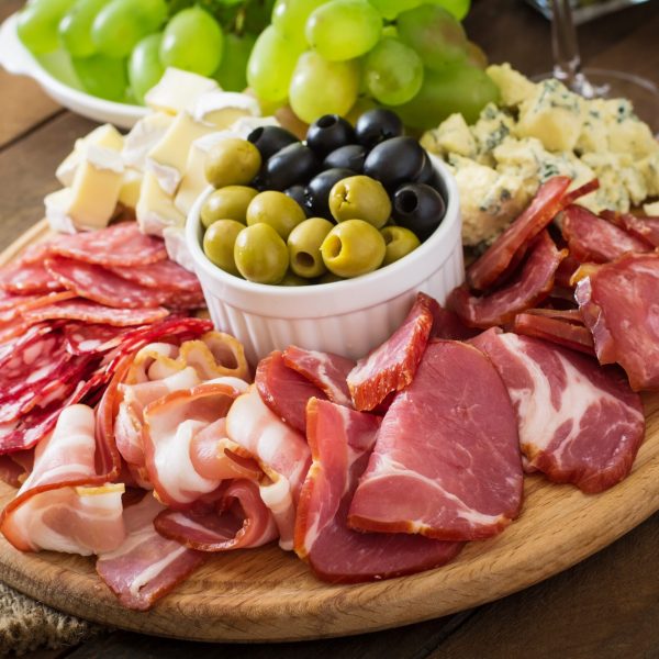 Antipasto catering platter with bacon, jerky, salami, cheese and grapes on a wooden background